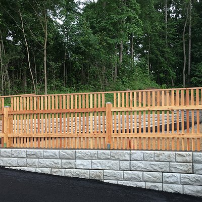 Beton-Stützwand mit Holzlattenzaun sichert den Hang entlang einer frisch asphaltierten Zufahrt
