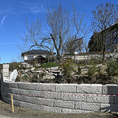 Betonmauer mit runder Form und Naturgarten am Hang eines Einfamilienhauses