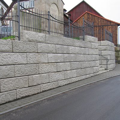 Strukturierte Betonsteine formen eine massive Mauer mit elegantem Verlauf entlang der Straße