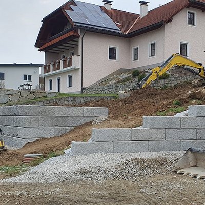 Gartenmauer aus strukturierten Betonsteinen in mehreren Stufen – Hang begradigt und Platz für den Hausgarten geschaffen