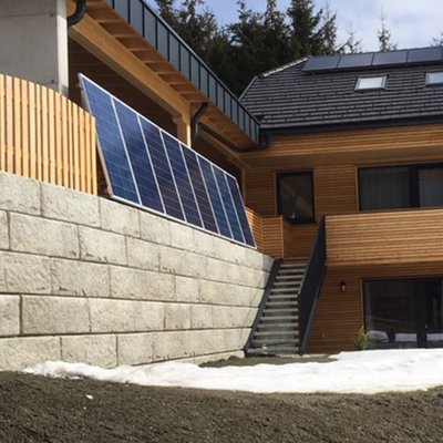 Massive Betonmauer sichert den Hang und schafft Platz für Solaranlage am modernen Holzhaus